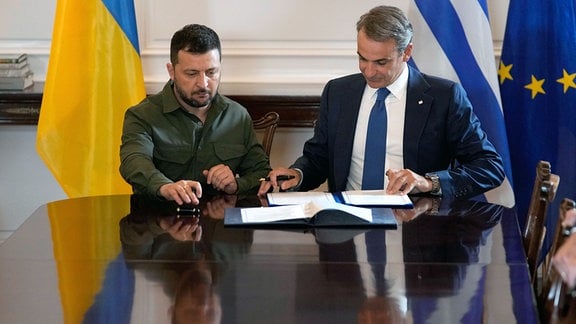 Wolodymyr Selenskyj (l), Präsident der Ukraine, und Kyriakos Mitsotakis, Ministerpräsident von Griechenland, unterzeichnen während ihres Treffens in der Maximos-Villa ein Abkommen. 