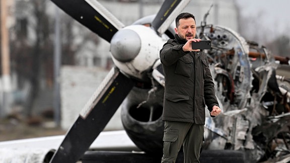 Selenskyj macht ein Foto vor einem Flugzeugwrack