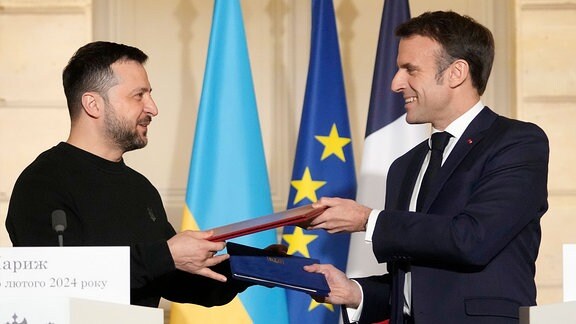 Emmanuel Macron (r), Präsident von Frankreich, und Wolodymyr Selenskyj, Präsident der Ukraine, tauschen nach der Unterzeichnung eines Abkommens im Elysee-Palast Dokumente aus. 