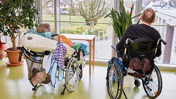 Im Rollstuhl sitzende Bewohner eines Pflegeheims schauen aus dem Fenster.