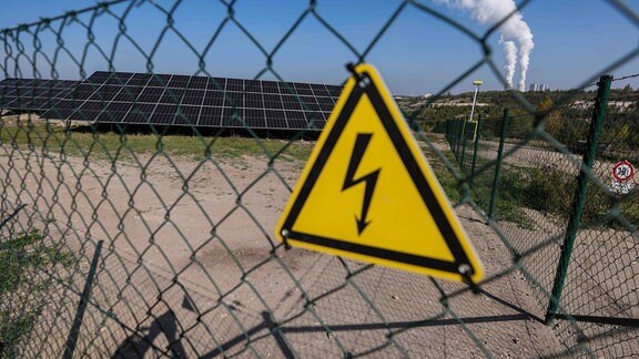 Ein Warnschild warnt vor Starkstrom an der neuen Photovoltaik-Anlage Peres II im ehemaligen Tagebau vor der Kulisse des Braunkohlekraftwerks Lippendorf. 