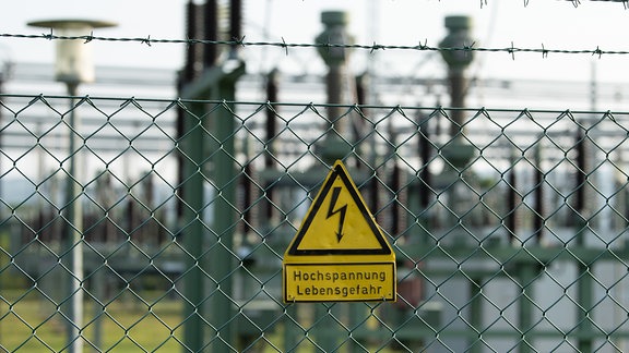 Ein Schild mit der Aufschrift „Hochspannung Lebensgefahr“ hängt an einem Zaun.