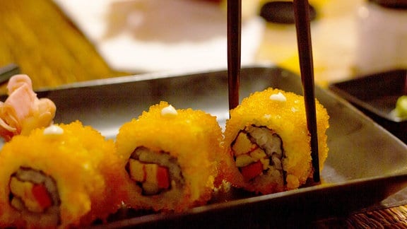 Essstäbchen, die Sushi-Rolle mit orangefarbenem Tobiko nehmen.