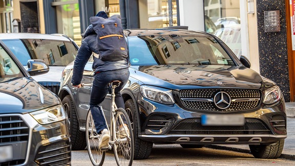 Ein*e Radfahrer*in bewegt fährt an geparkten SUVs vorbei.