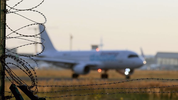 Ein Flugzeug startet auf dem Flughafen Frankfurt a.M., im Vordergrund ein Sicherheitszaun mit Stacheldraht.