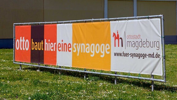 "Otto baut hier eine Synagoge" steht auf einem Banner das über eine Wiese gespannt ist.