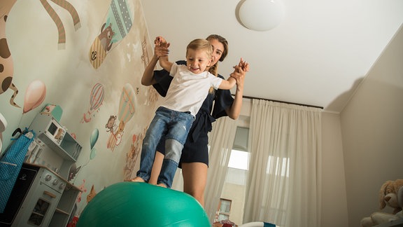 Eine Frau spielt mit einem Jungen auf einem Gymnastikball.