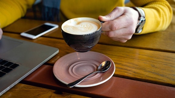 Mann hält Kaffeetasse neben Laptop im Café.