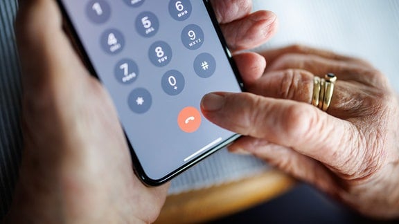 Eine über 90-jährige Frau drückt auf ihrem Smartphone während eines Telefongesprächs auf die rote Schaltfläche zum Beenden des Anrufs.