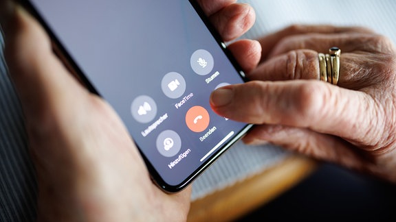 Eine über 90-jährige Dame drückt auf ihrem Smartphone während eines Telefongesprächs auf die rote Schaltfläche zum Beenden des Anrufs.