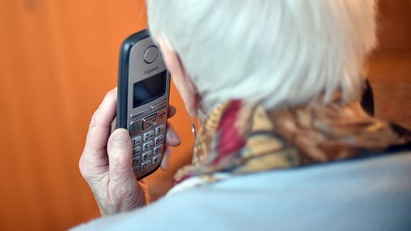 Eine Seniorin hält einen Telefonhörer an ihr Ohr (gestellte Szene).