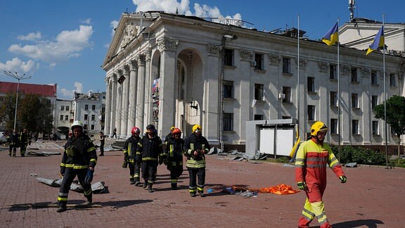 Feuerwehrleute gehen neben dem akademischen ukrainischen Musik- und Dramatheater Tschernihiw, das durch einen Angriff beschädigt wurde.