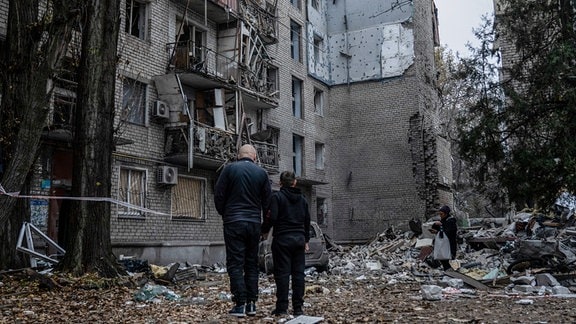 Zwei Anwohner stehen vor den Trümmern eines Gebäudes. Bei einem neuen Raketenangriff auf die Ukraine hat Russland nach Angaben aus Kiew ein Wohnhaus in der Stadt Mykolajiw zerstört. Der ukrainische Gouverneur Kim teilte am Morgen im Nachrichtenkanal Telegram mit, es seien mehrere Tote aus den Trümmern des fünfgeschossigen Wohnhauses geborgen worden.