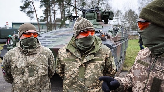 Drei Ukrainische Soldaten stehen vor einem Schützenpanzer Marder.