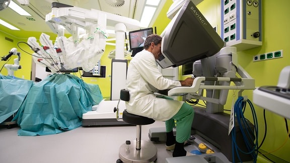 Jürgen Weitz sitzt in einem Experimental-OP-Saal an einem Da-Vinci-Operationssystem für minimalinvasive Operationen.