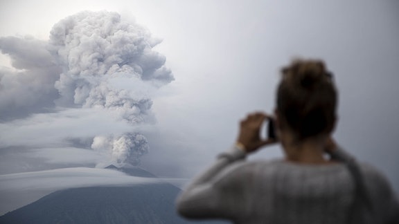 Ein Mann fotografiert am 28.11.2017 in Karangasem auf Bali (Indonesien) den Vulkan Mount Agung, der Rauch und Asche spuckt. Wegen der Gefahr eines unmittelbar bevorstehenden Ausbruchs des Vulkans gilt auf Bali derzeit die höchste Alarmstufe. 