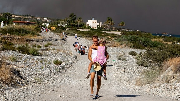 Ein Mann trägt ein Kind, als sie ein Gebiet verlassen, in dem ein Waldbrand auf der griechischen Insel Rhodos wütet. 