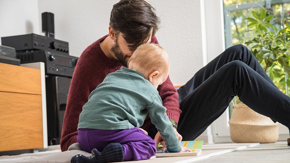 Ein Vater schaut in einer Wohnung in Berlin mit seinem Kind in einem Bilderbuch