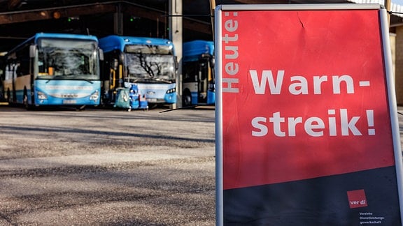 Busse der Verkehrsbetriebe Plön stehen hinter einem Schild mit der Aufschrift „Warnstreik“ auf dem Betriebshof in Preetz. 