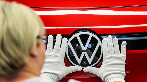 Eine Mitarbeiterin prüft das VW-Logo an einem ID.4 im Lichttunnel im Werk von Volkswagen in Zwickau.
