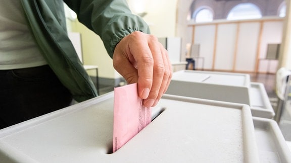 Eine Person wirft einen Stimmzettel in eine Urne.