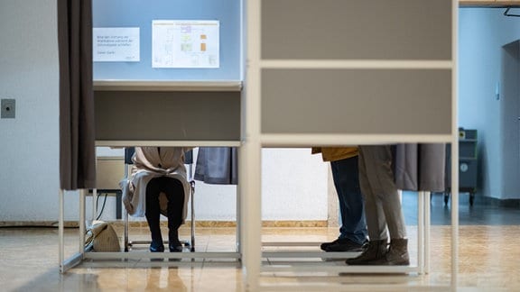 Zwei Wählerinnen und ein Wähler füllen in einem Wahlbüro im Rathaus der baden-württembergischen Landeshauptstadt Wahlunterlagen aus.
