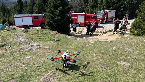 Eine Flugdrohne steht auf einer Wiese, im Hintergrund Einsatzfahrzeuge der Feuerwehr.