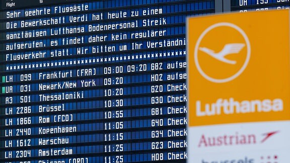 Eine Anzeigetafel mit Informationen über den Streik und das Logo der Lufthansa sind am Flughafen München zu sehen. 