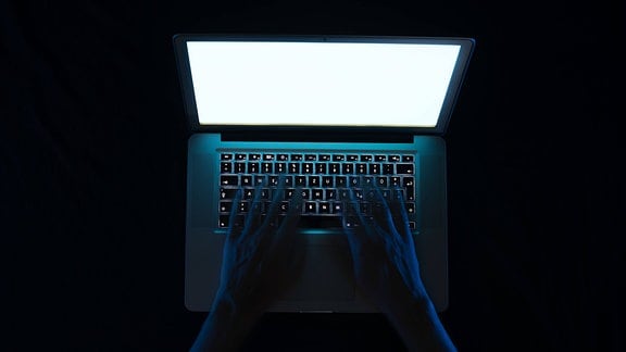 Aus einem Laptopbildschirm wird eine Person am Rechner von einem Kriminellen mit der ausgestreckten Hand bedroht
