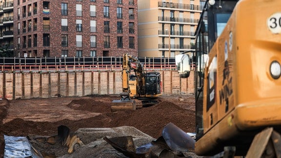 Bagger stehen in einer Baugrube vor neugebauten Wohnungen.