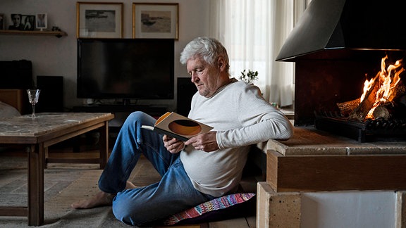 Ein Mann lehnt lesend an einem Kaminofen.