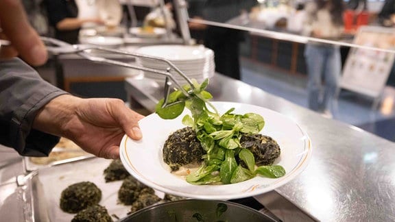 Ein Mitarbeiter bereitet einen Teller „Spinatknödel auf Pilzragout mit Feldsalat“ in der neuen Mensa „Blattwerk“ auf dem Campus Von-Melle-Park der Universität Hamburg vor. 