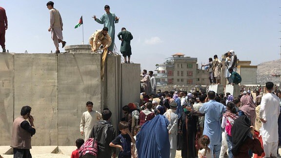 Menschen versuchen die Mauer des Flughafens ins Kabul zu überwinden.