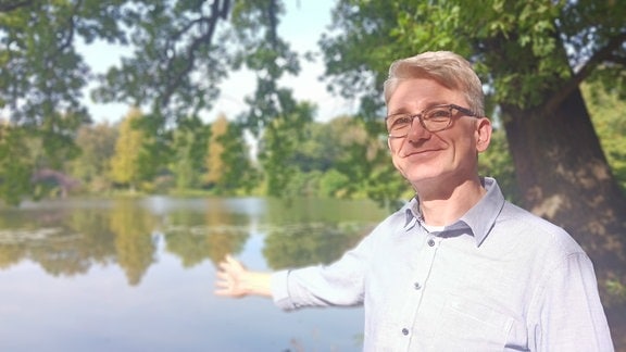 Porträt Michael Keller: Ein Mann mit Brille steht vor einem Teich im Gartenreich Dessau-Wörlitz.