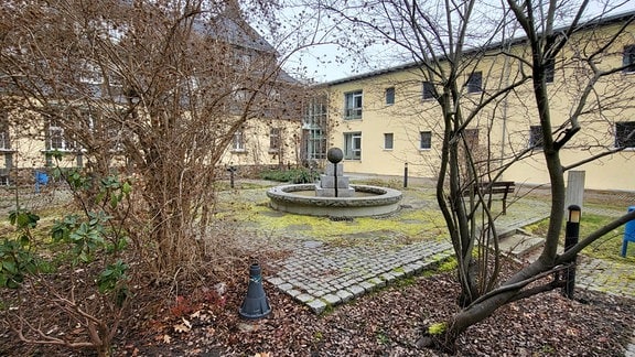 Innenhof des Versorgungszentrums in Schneeberg mit Sträuchern und altem Trinkbrunnen aus Stein. 