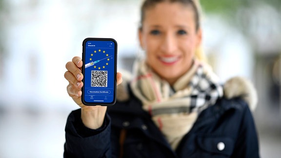 Frau zeigt Smartphone mit digitalem europäischen Impfpass mit QR-Code