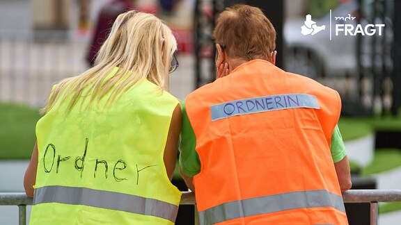 Ordner und Ordnerin steht auf Sicherheitswesten zweier Personen die nebeneinander stehen.