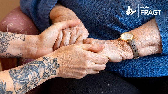Hände einer Altenpflegerin halten liebevoll die Hände einer Seniorin