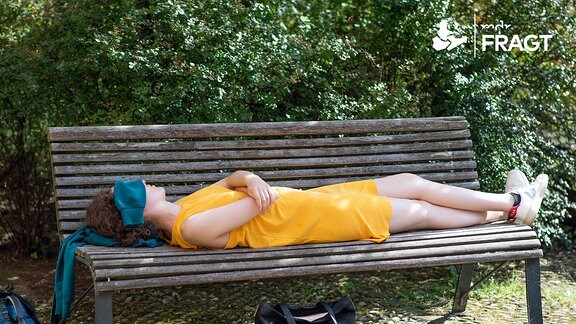 Eine Frau liegt auf einer Bank im Schatten, im Gesicht bedeckt mit einem Tuch geschützt von der Sonne. 