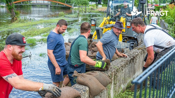 Helfer beseitigen Sandsäcke am Ufer der Paar.