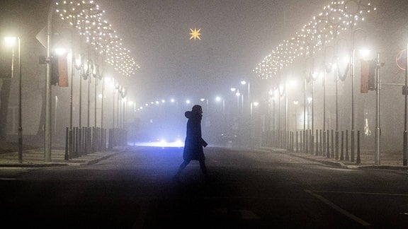 Eine Frau läuft entlang einer mit Weihnachtsbeleuchtung geschmückten Strasse im Nebel in Niesky.