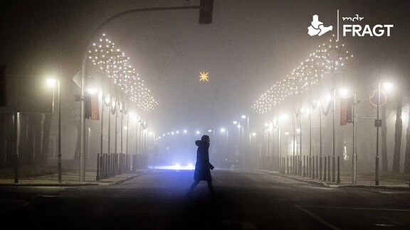 Eine Frau läuft entlang einer mit Weihnachtsbeleuchtung geschmückten Straße im Nebel in Niesky.