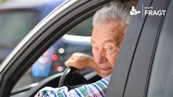 Rentner am Steuer eines PKWs schaut aus dem heruntergelassenen Seitenfenster.