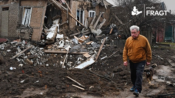 Ein Mann geht spazieren vor einem zerstörten Wohnhaus