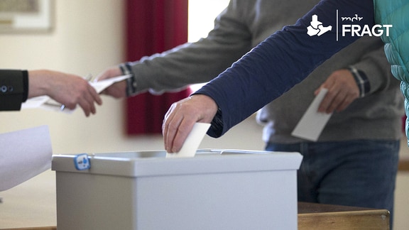 Ein Wähler steckt im Wahlbuero ein Wahlumschlag in eine Wahlurne.