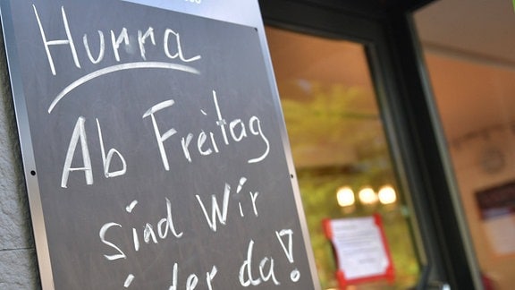 Auf Restauranttafel steht mit Kreide geschrieben: 'Hurra - Ab Freitag sind wir wieder da!'