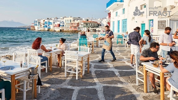 Urlauber und Kellner auf der Terasse eines Strandrestaurants auf Mykonos