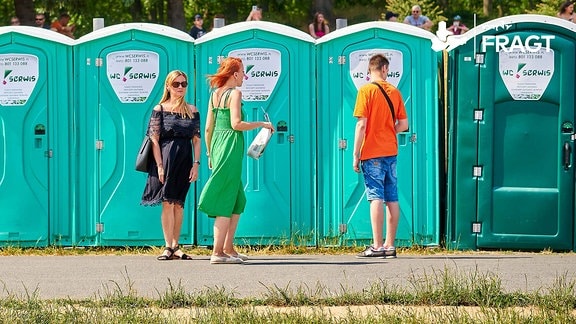 Zwei Frauen und ein Mann stehen vor einer Reihe von mobilen Toilettenkabinen