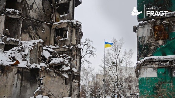 Eine ukrainische Flagge weht auf einem Mast in der Nähe der Ruinen eines von russischen Truppen zerstörten Wohnhauses
