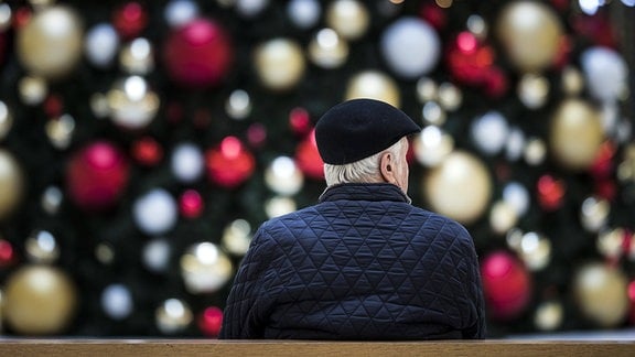 Ein Mann sitzt allein auf einer Bank vor einem geschmückten Weihnachtsbaum